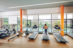 Fit young woman running on treadmill in empty gym, view from the back