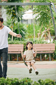 Father pushing his adorable little daughter sitting on swing in park