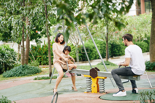 Young mother, father and daughter playing on seesaw in park