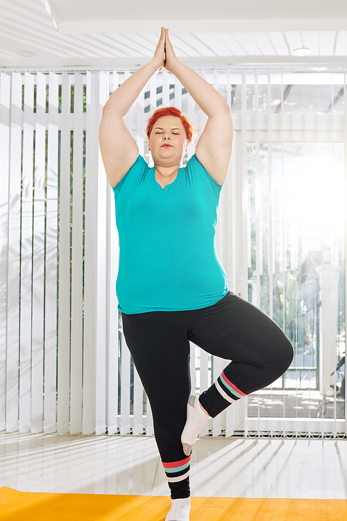 Plus size young woman balancing in tree position with her eyes closed