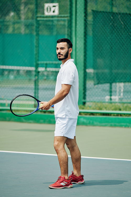 Handsome young Hispanic man in white sports clothing playing tennis outdoors