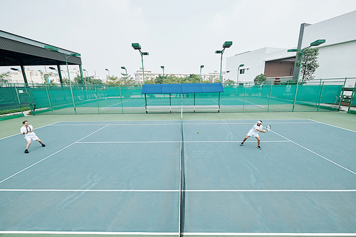 Friends in white sportswear playing game of tennis on outdoor court