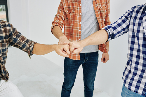 Three unrecognizable men wearing casual outfits with checked shirts bumping their fists in symbol of unity and friendship, high angle shot