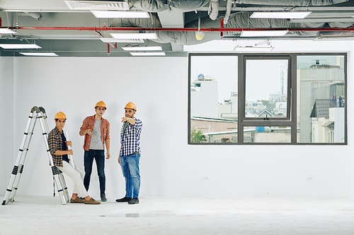 Group of construction engineers coworking in spacious unfinished building room, horizontal long shot, copy space
