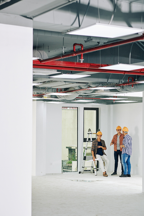 Long shot of three professional construction workers spending time in unfinished room having lively discussion, copy space