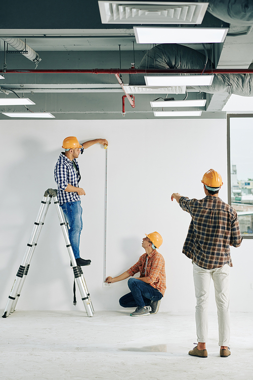 Vertical long shot of professional construction workers taking length measurements using tape rule, copy space