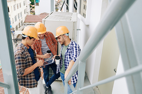 Group of three manual workers drinking coffee, using digital tablet and chatting during break at work, high angle shot