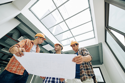 Horizontal low angle shot of professional manual workers wearing hardhats holding construction plan paper, copy space
