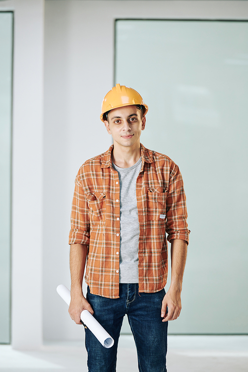 Portrait shot of modern construction worker wearing casual outfit and protective hardhat looking at camera