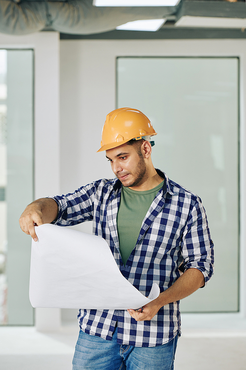 Portrait of professional construction engineer with serious facial expression looking into building plan paper