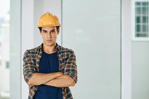 Waist up portrait of serious construction specialist wearing checked shirt and protective hardhat standing with arms crossed looking at camera