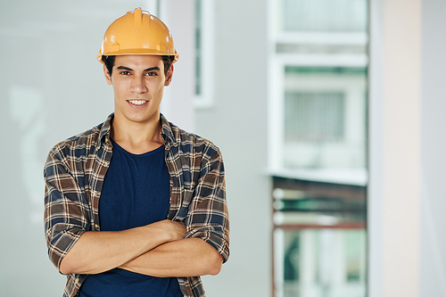 Waist up portrait of handsome construction engineer wearing casual clothes and protective hardhat standing with arms crossed looking at camera smiling, copy space