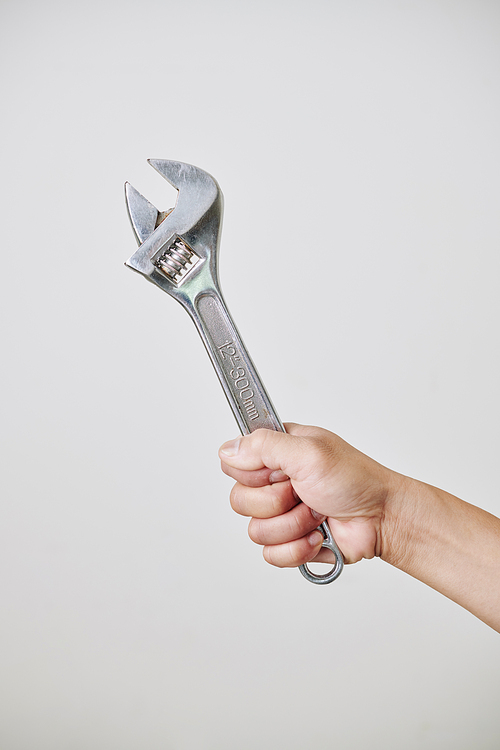Hand of builder or construction worker holding adjustable wrench, isolated on light grey