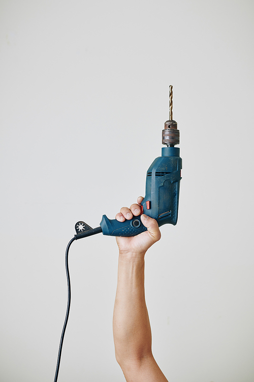 Professional builder raising hand with electric drill, isolated on light grey
