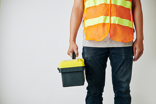 Repairman in bright vest standing with toolbox against light grey background