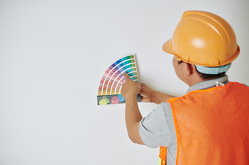 Construction worker in hardhat and orange vest choosing color from palette with swatches
