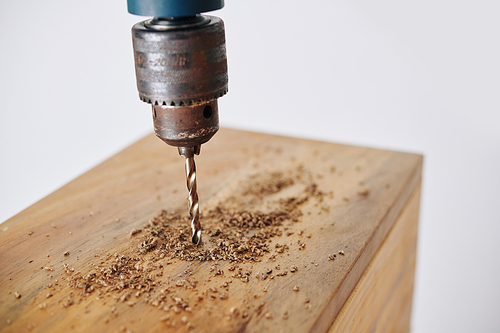 Close-up image of electric drill making hole in wooden plank when making furniture in workshop