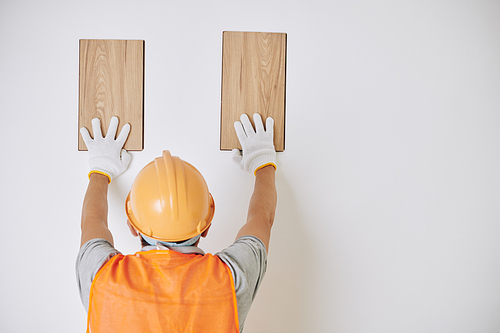 Builder in hardhat and textile gloves choosing what wooden planks to use for wall decoration