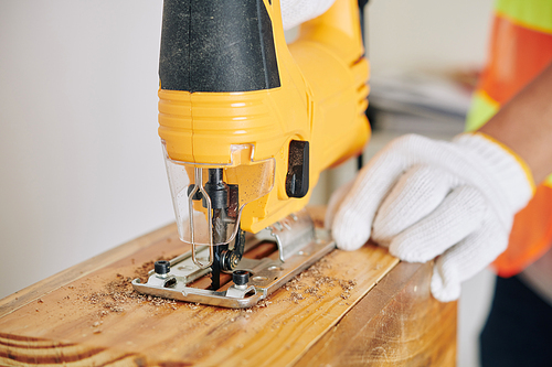 Close-up image of carpenter using jigsaw for cutting wooden plank when making furnutire
