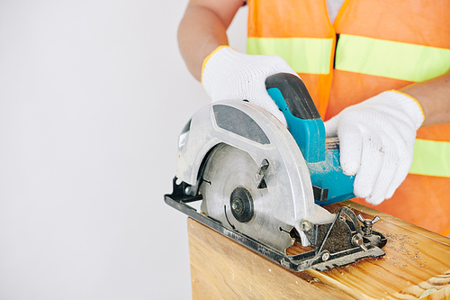 Close-up image of construction worker cutting wooden plank with electric saw