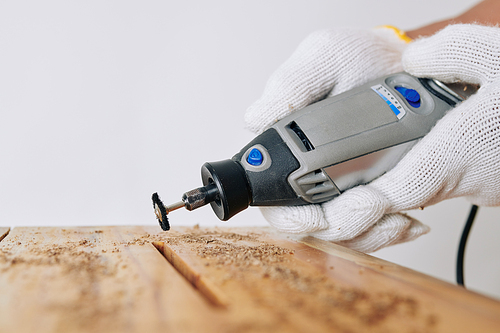 Professional carpenter using rotary hand tool to clean elongated hole in stool or other piece of furniture