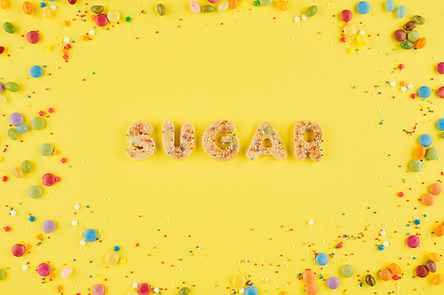 Sweet cookie word sugar on bright yellow background with colorful sprinkles, view from the top