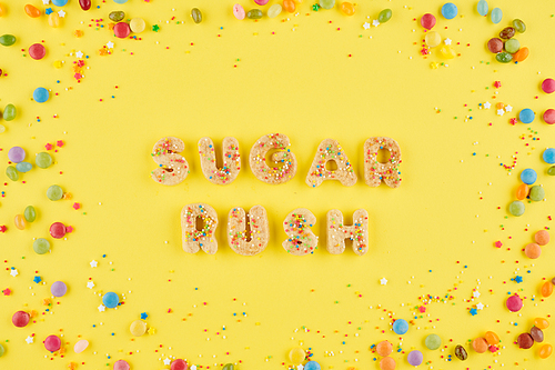 Words sugar rush from cookie alphabet on bright yellow background with colorful candies