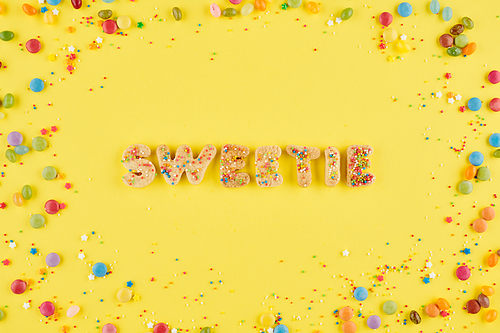 Sweetie word from baked cookie letters with sprinkles and candies around