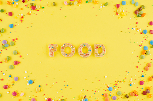 Word food arranged from homemade sugar cookies on yellow background wih sprinkles and candies