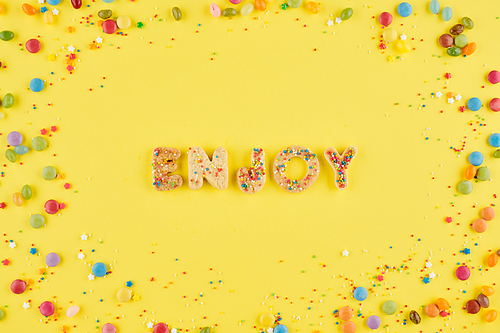 Enjoy word arranged from baked decorated cookies, sprinkles and small candies around