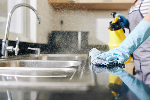 Close-up image of woman spraying disinfecting detergent on kitchen counter and sink to kill all bacteria