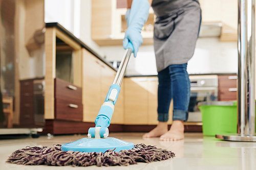 Housewife enjoying spring cleaning and mopping kitchen floor with mop, selective focus