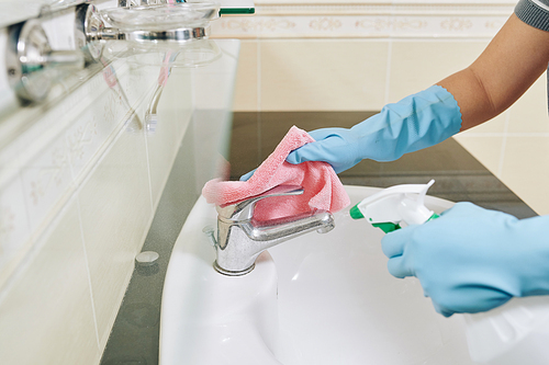 Housewife wearing rubber gloves when wiping faucet in bathroom with soft cloth and detergent