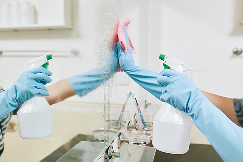 Woman in rubber gloves cleaning bathroom mirror with glassware detergent