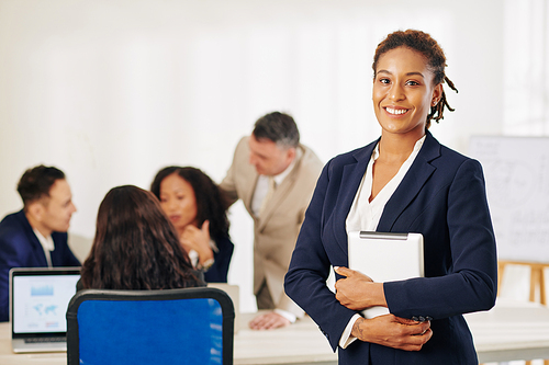 Successful Hispanic young businesswoman with tablet computer in hands standing in meeting room