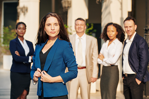 Portrait of young serious businesswoman standing outdoors in front of her colleagues