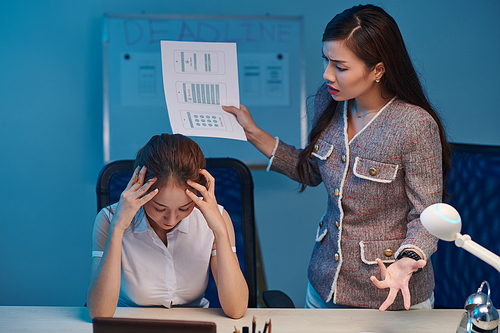 Female project manager telling off UI designer for bad work when staying late in office on night before deadline