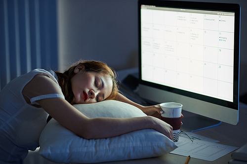 Exhausted young female businesswoman fell asleep in office in front of glowing computer screen with working calendar on it