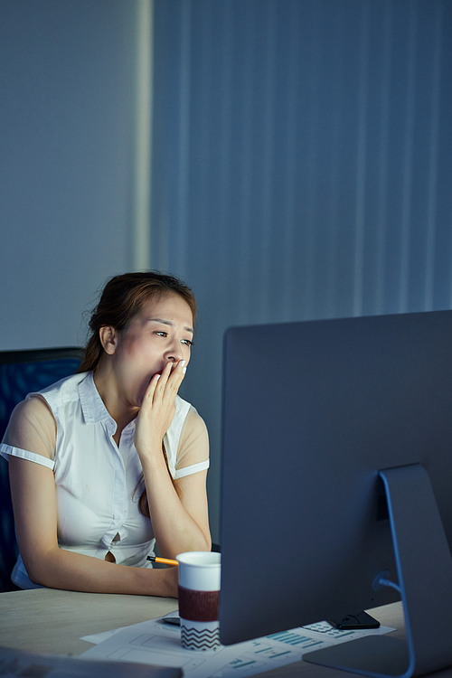 Yawning young businesswoman covering mouth with hands tired of working on computer all night long