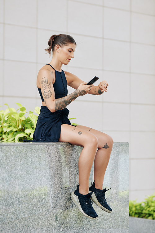 Female jogger sitting on parapet and checking pulse tracker on her wrist