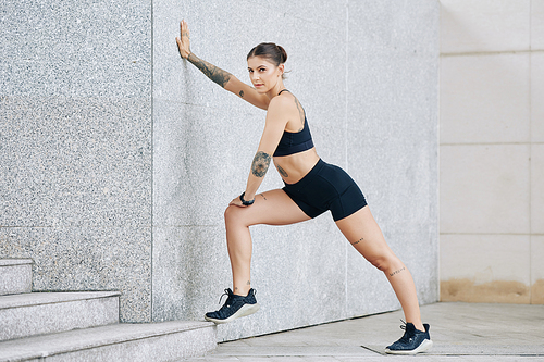 Woman leaning on wall when doing leg stretch after running in the street