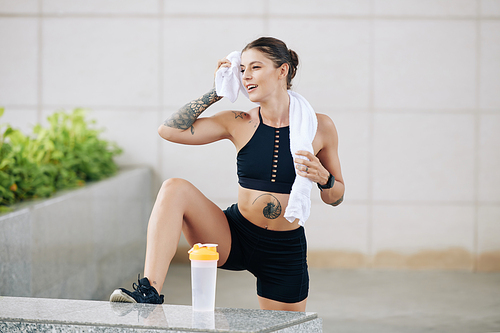 Smiling fit young woman in top and shorts wiping off sweat after intense training