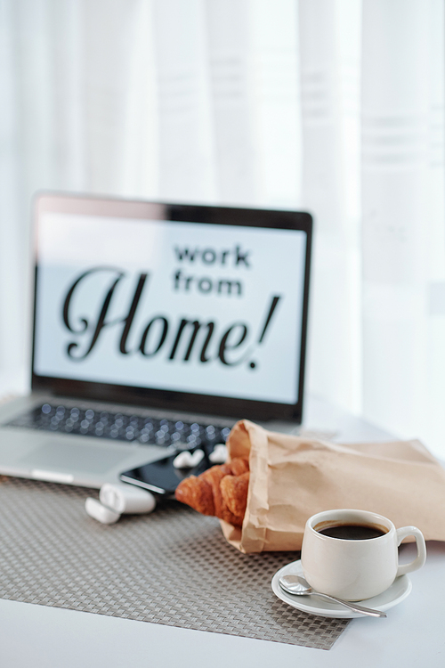 Opened laptop, cup of morning coffee anf fresh croissants from local bakery on table of person working from home during covid19 lockdown