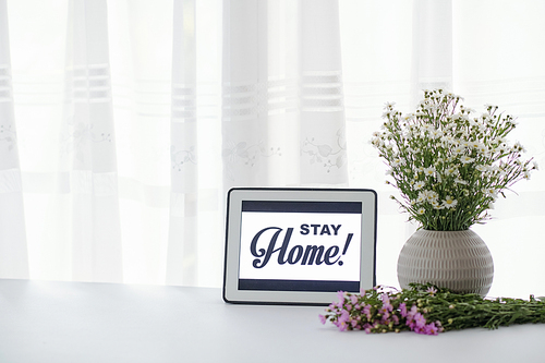 Vase with fresh wild flowers and digital tablet with stay home inscription
