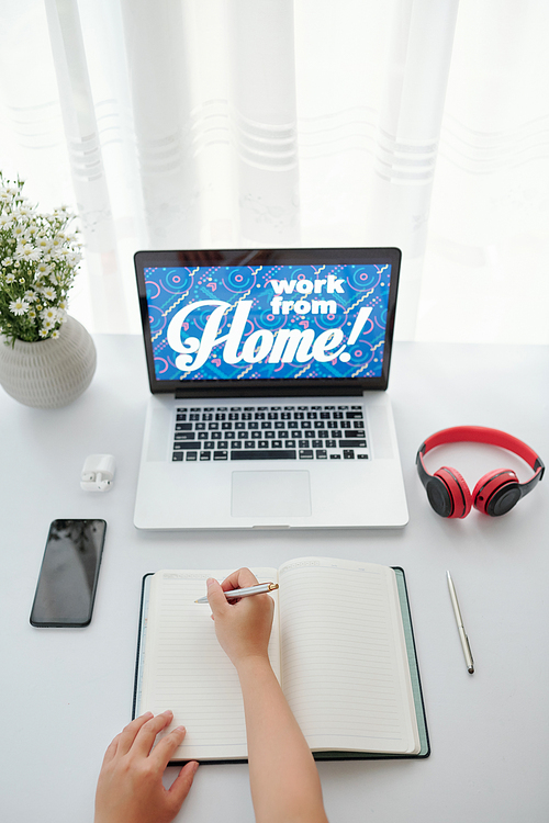 Business person working from home during quarantine and taking notes in planner, view from above