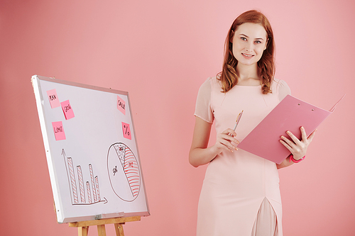 Portrait of cheerful young businesswoman standing at whiteboard when conducting presentation for colleagues