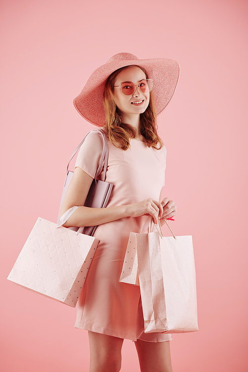 Studio portrait of smiling pretty young woman with shopping bags posing against pink background