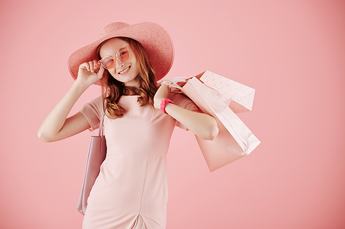 Portrait of smiling lovely young woman in sunglasses and straw hat posing with shopping bags