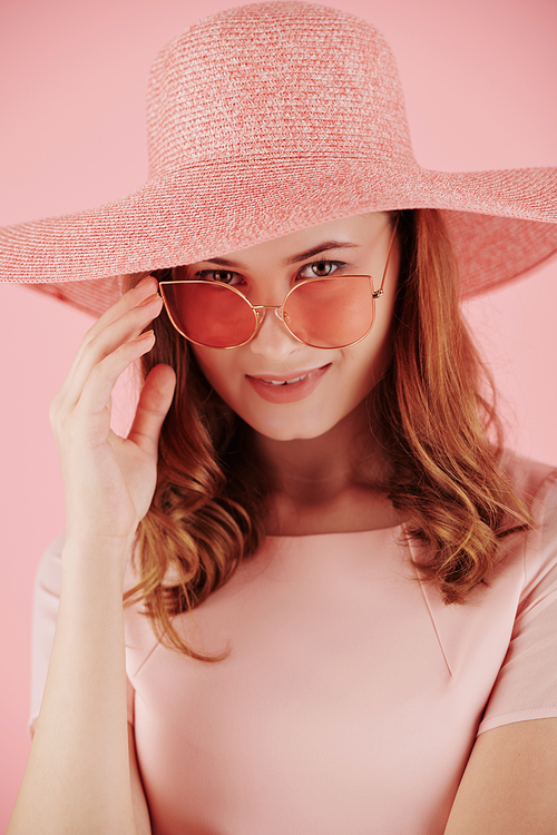 Portrait of smiling yuong red haired woman pink pink hat taking off sunglasses and looking at camera