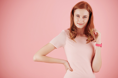 Portrait of lovely smiling red haired young woman in light pink dress posing against pink backgrounf